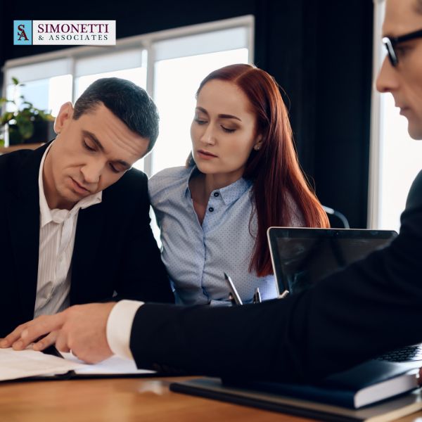 A man and woman review documents with a professional at an office desk; the Simonetti & Associates logo is visible in the top left corner, highlighting their reputation as the best divorce lawyer on Long Island.