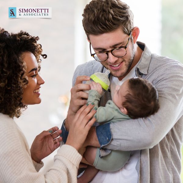 A woman and man smile while the man holds and bottle-feeds a baby; the Simonetti & Associates logo is in the top left corner, highlighting your trusted Huntington divorce lawyer.