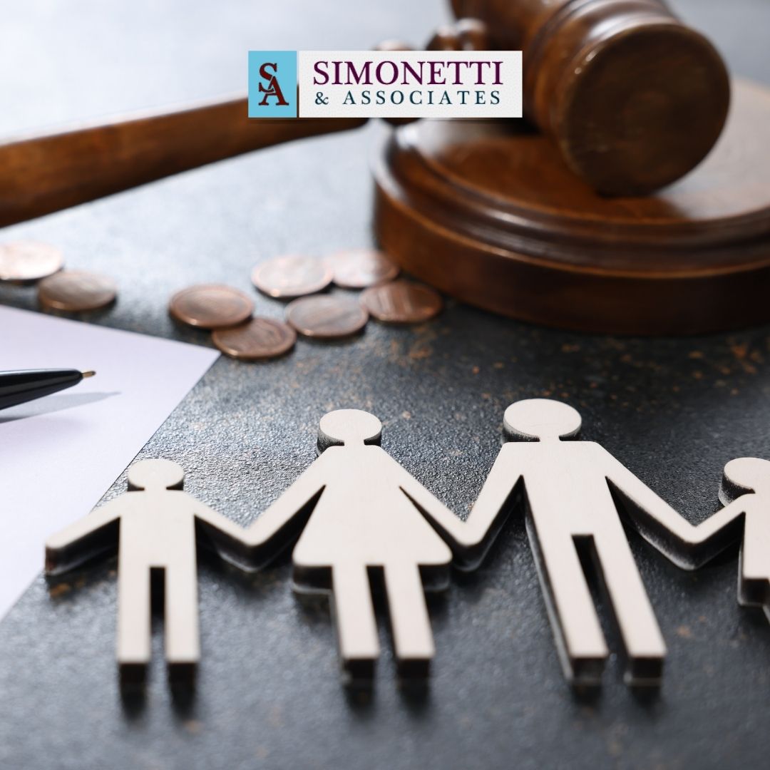 Wooden cutouts of a family, a gavel, coins, and paperwork with a pen on a desk, featuring the Simonetti & Associates logo in the background—representing trusted guidance from your Massapequa Divorce Lawyer.