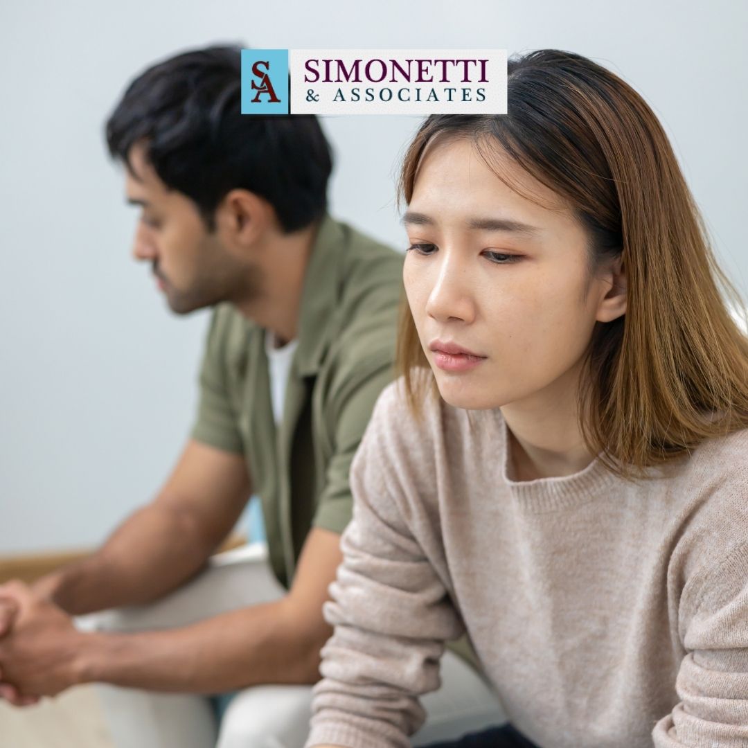 A woman and a man sit apart looking serious or thoughtful; above them, the "Simonetti & Associates" logo appears, highlighting their reputation as a trusted divorce lawyer in Huntington.