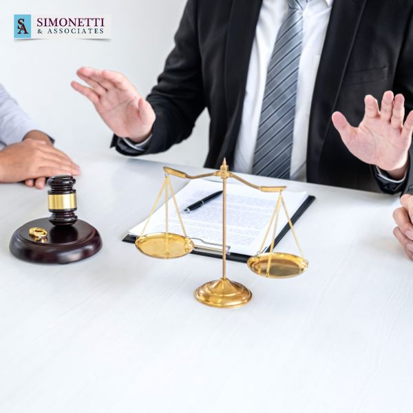 Three people sit at a table with legal documents, a gavel, and scales of justice; a Divorce Lawyer in Massapequa gestures with raised hands.