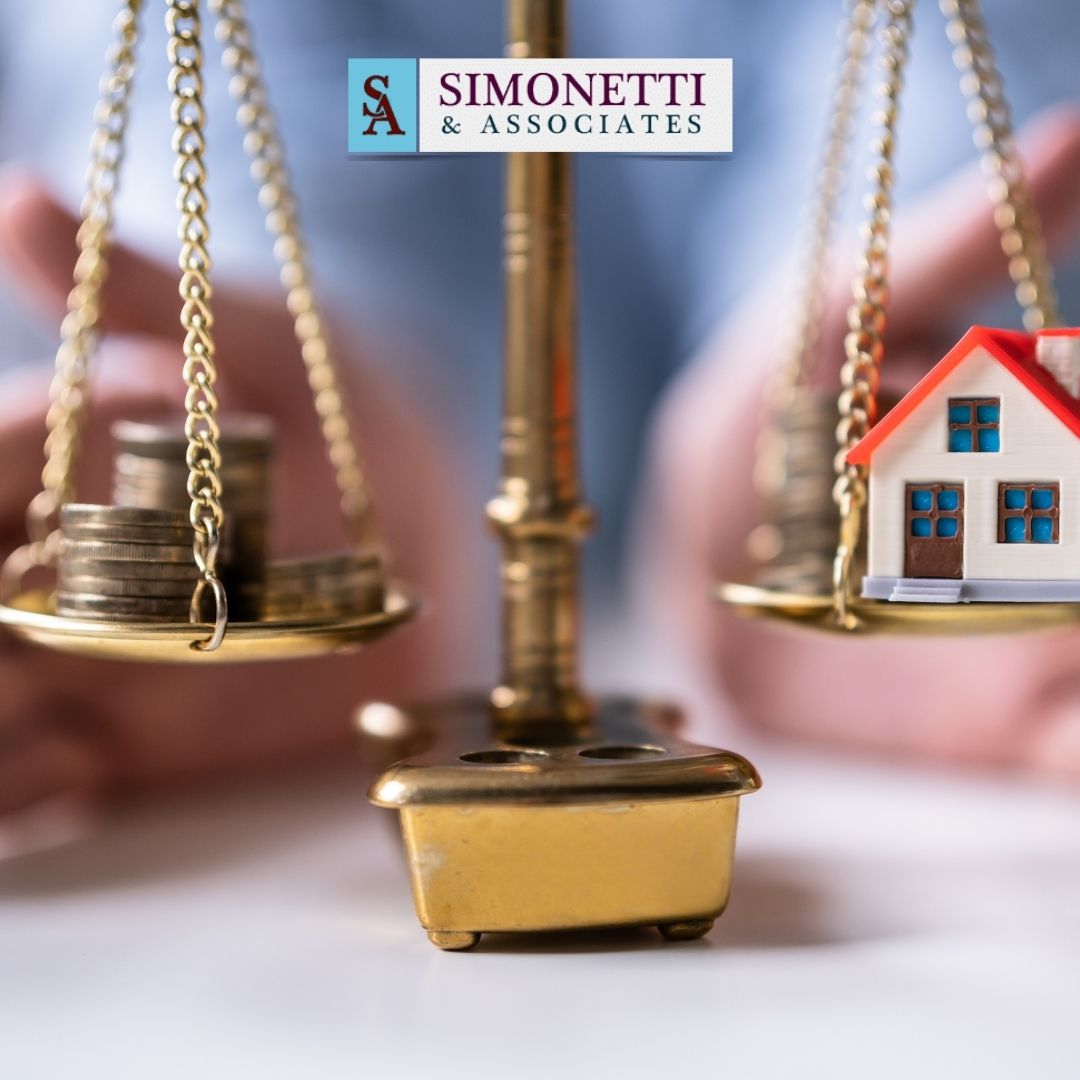 A scale balances stacks of coins on one side and a small house model on the other, with hands in the background and a "Simonetti & Associates" logo above, highlighting the role of a Massapequa Divorce Lawyer in property division.