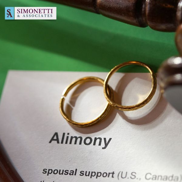 Two gold wedding rings rest on a document labeled "Alimony" with the Simonetti & Associates logo in the top left corner, symbolizing matters an experienced divorce attorney in Nassau County can help address.