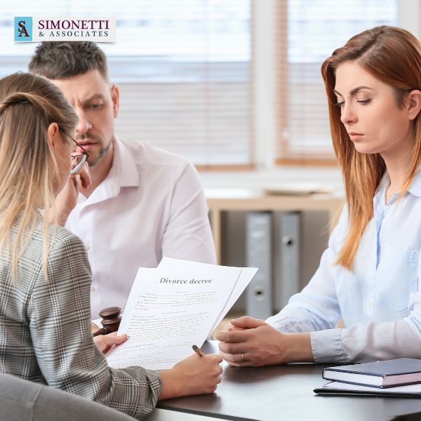Three people sit at a desk reviewing a divorce decree document with a Nassau Divorce Lawyer; a woman holds the paper while the other two listen seriously.