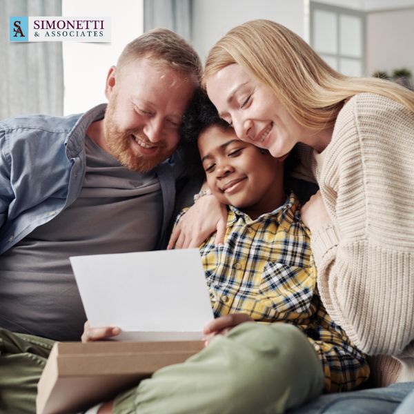 A smiling man, woman, and child sit close together looking at a piece of paper, with a Simonetti & Associates logo in the top left corner—illustrating the care and guidance of a trusted Long Island Family Lawyer.