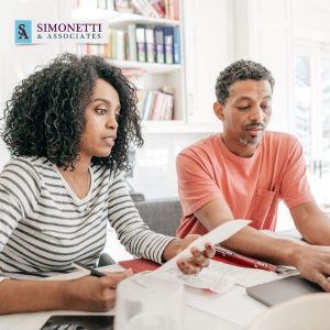 A woman and man sit at a table reviewing documents together in a bright office with the Simonetti & Associates logo in the corner, consulting with a Divorce Lawyer in East Hampton.