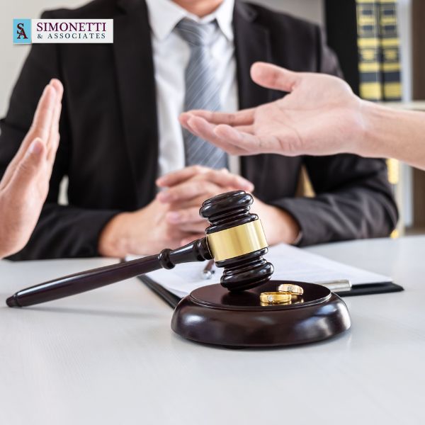 Two people sit across from each other with a gavel and wedding rings on the table, suggesting a legal discussion about divorce or separation, with a divorce lawyer in Water Mill present.