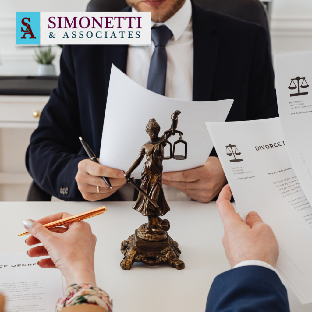 Three people discuss divorce documents at a table with a Lady Justice statue in the center and a Simonetti & Associates logo in the background, highlighting Suffolk County Family Esq. expertise.