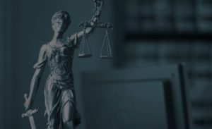 A close-up of a Lady Justice statue holding balanced scales and a sword, with a blurred background.