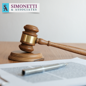 A judge's gavel and a pen rest on a desk with documents, with the Simonetti & Associates logo displayed in the upper left corner, representing your trusted Divorce Lawyer in Commack.