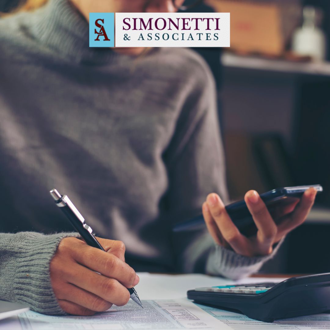 A person fills out forms using a pen and calculator, with the Simonetti & Associates logo above—highlighting the trusted divorce lawyer in Nassau County.