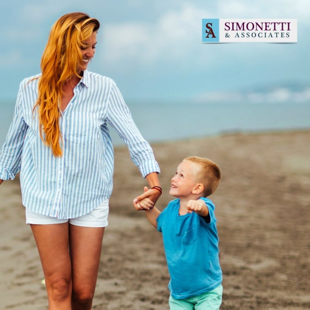 A woman and a young boy hold hands and walk on a beach. Logo for Simonetti & Associates appears in the top right corner.