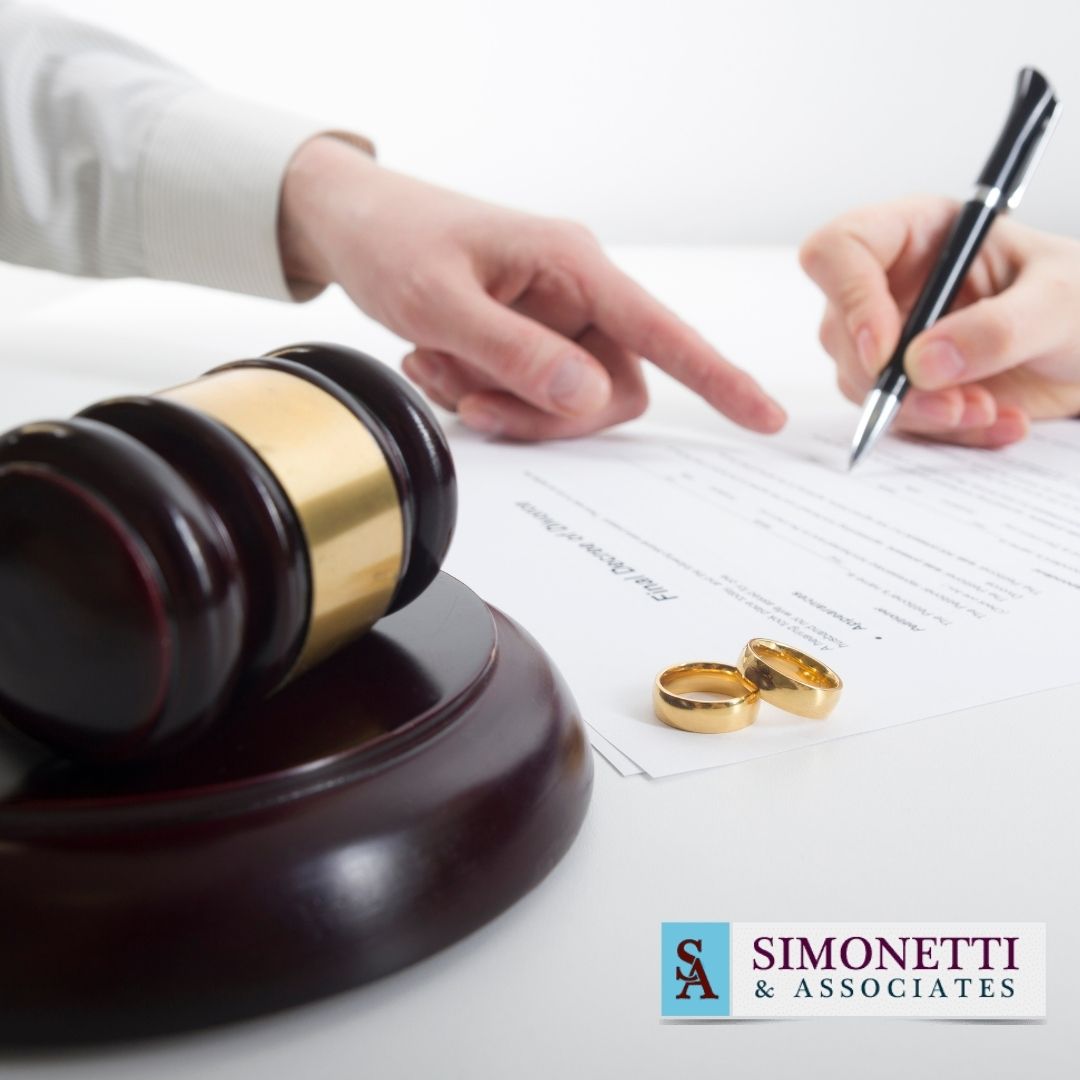 Two people review and sign divorce papers next to a judge’s gavel and wedding rings, with the Simonetti & Associates logo in the corner—trusted Divorce Lawyer in Lake Grove.